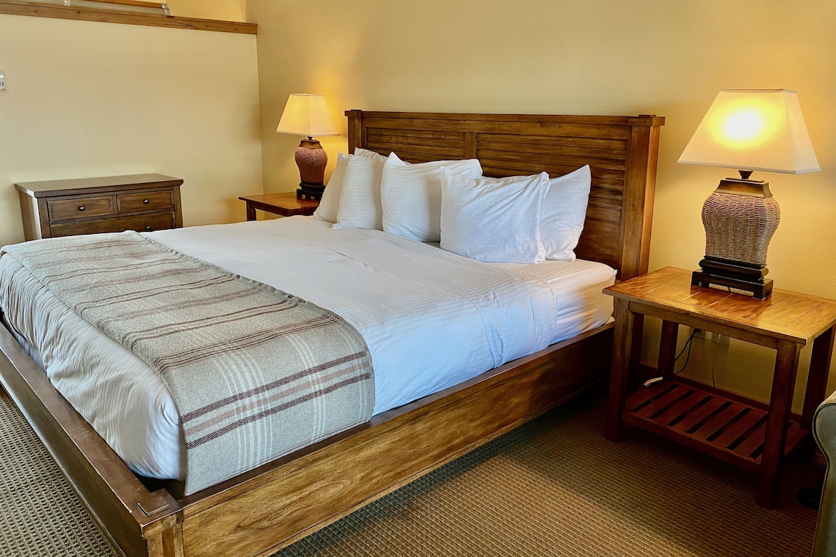 A neatly made bed with white linens, a wooden headboard, and two bedside lamps.