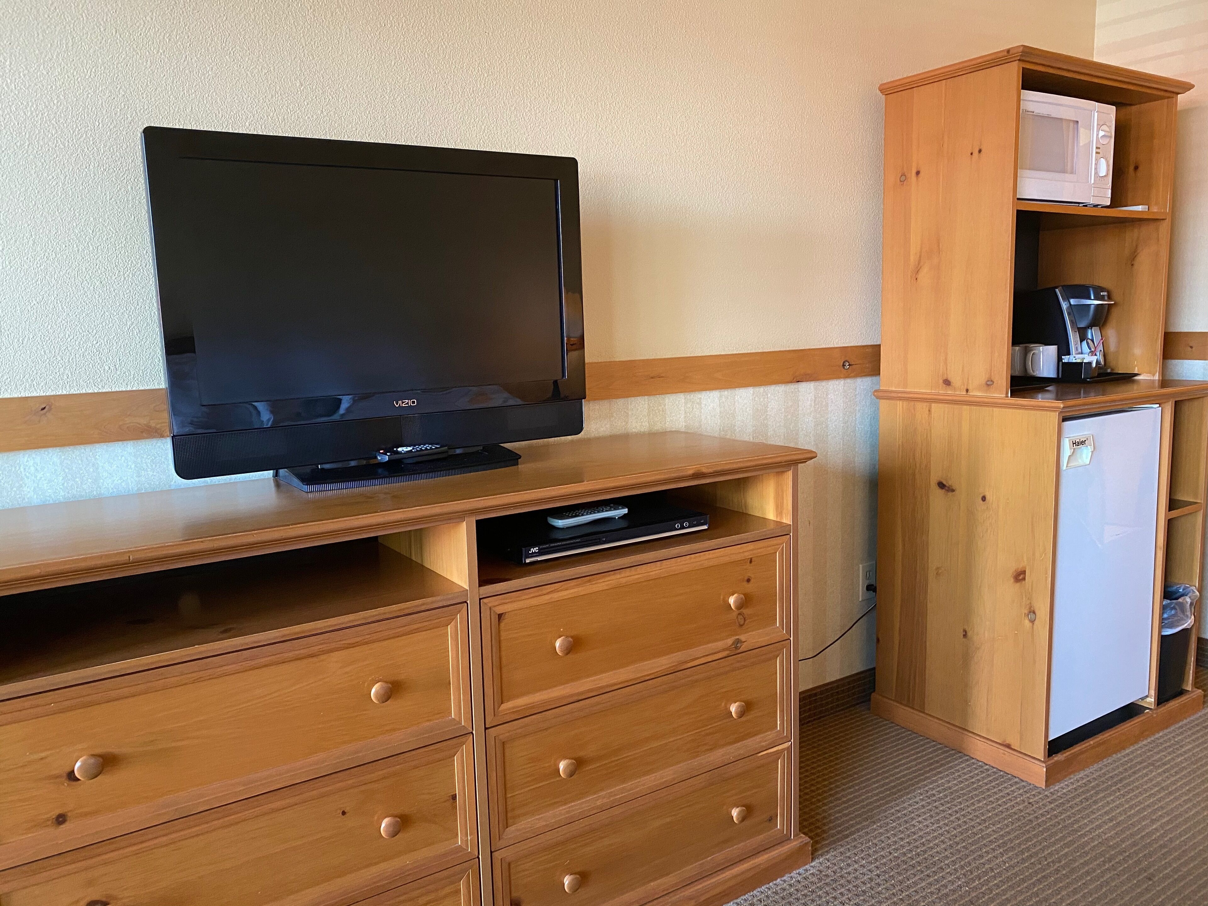 Una habitación con un televisor sobre un soporte de madera, un mueble de madera con un microondas y un refrigerador pequeño.