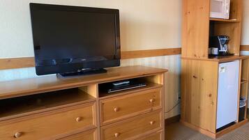 Una habitación con un televisor sobre un soporte de madera, un mueble de madera con un microondas y un refrigerador pequeño.