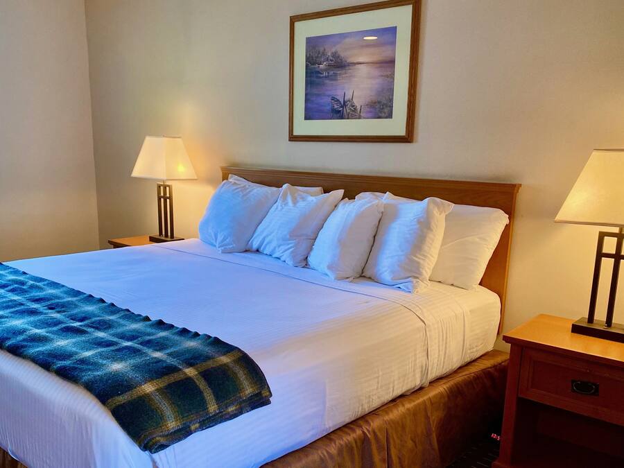 A neatly made bed with white linens, a blue plaid blanket, and two bedside lamps.