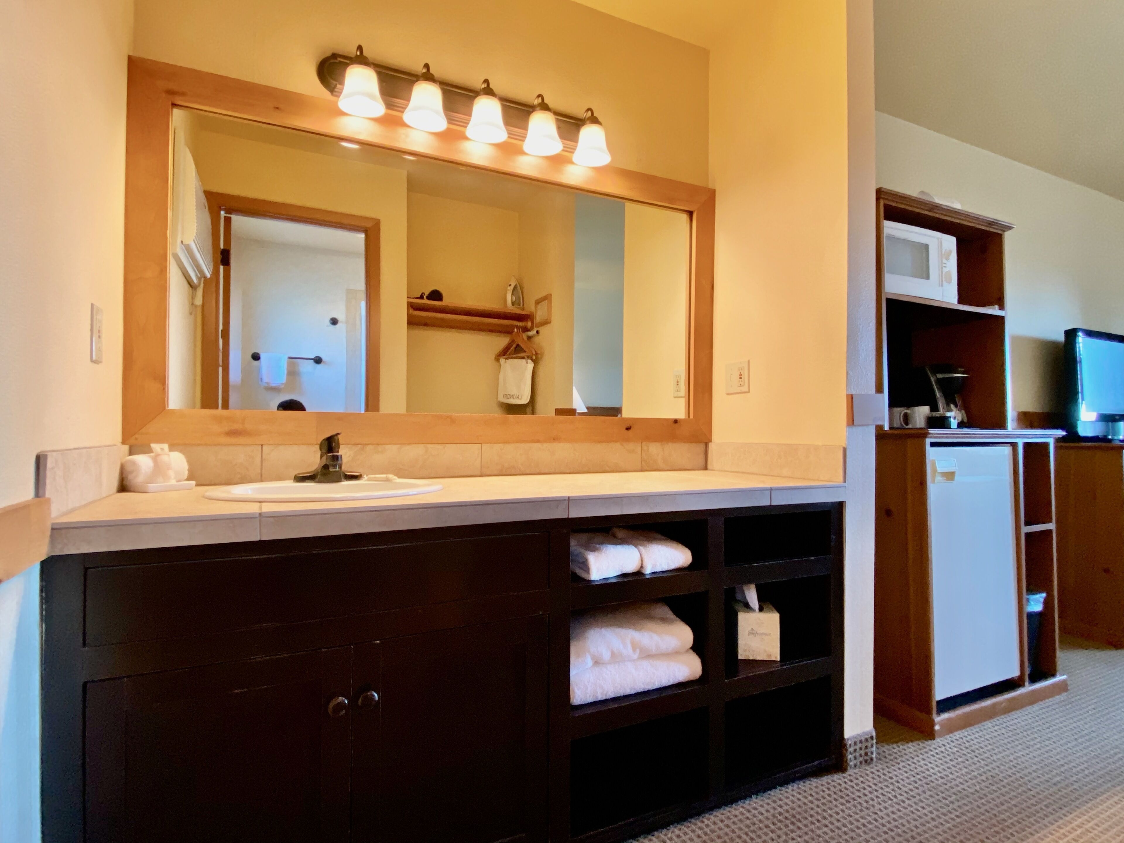 A bathroom with a large mirror, a sink, and a dark wooden cabinet with towels.