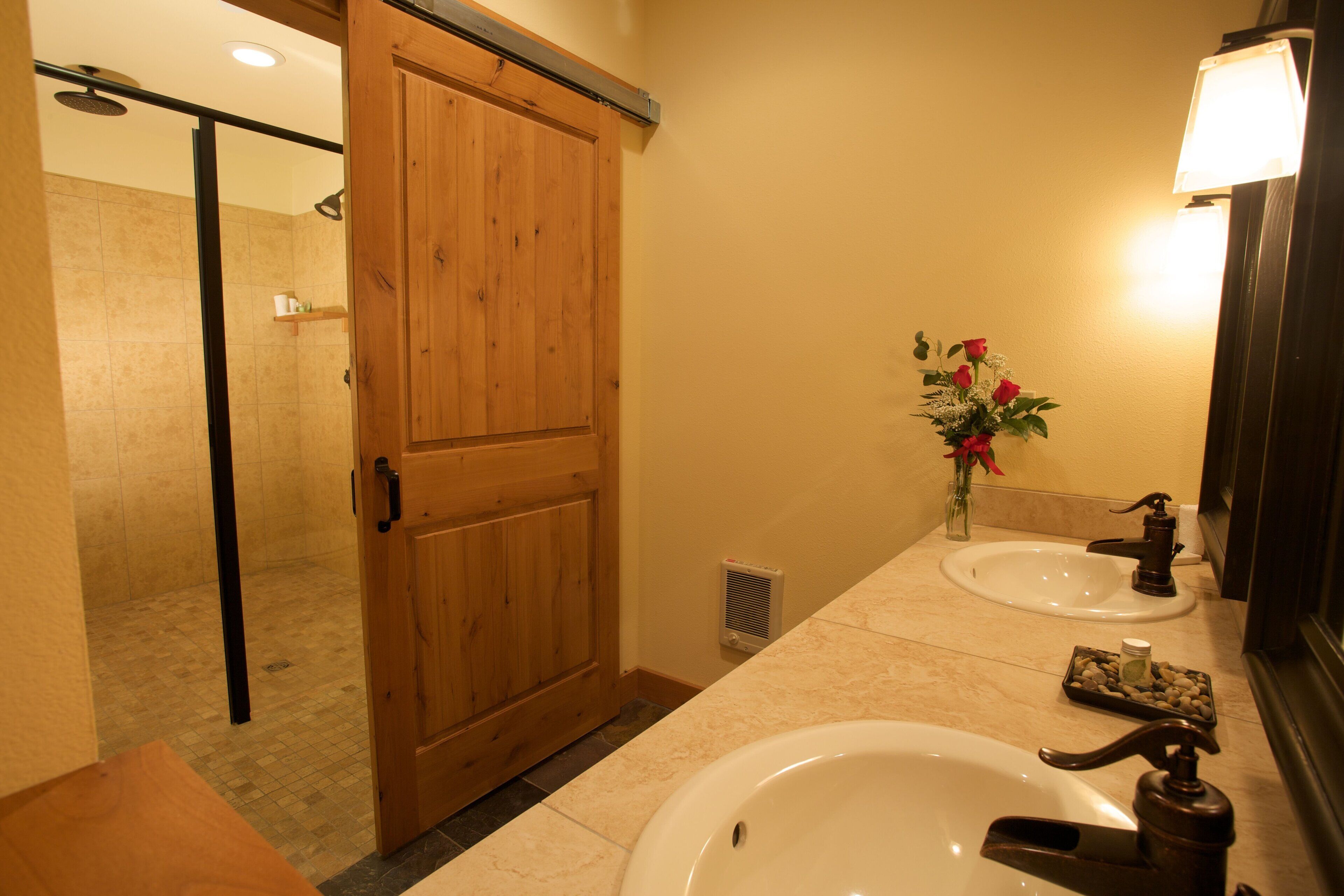 Un baño con puerta de madera, lavamanos, espejo y zona de ducha.