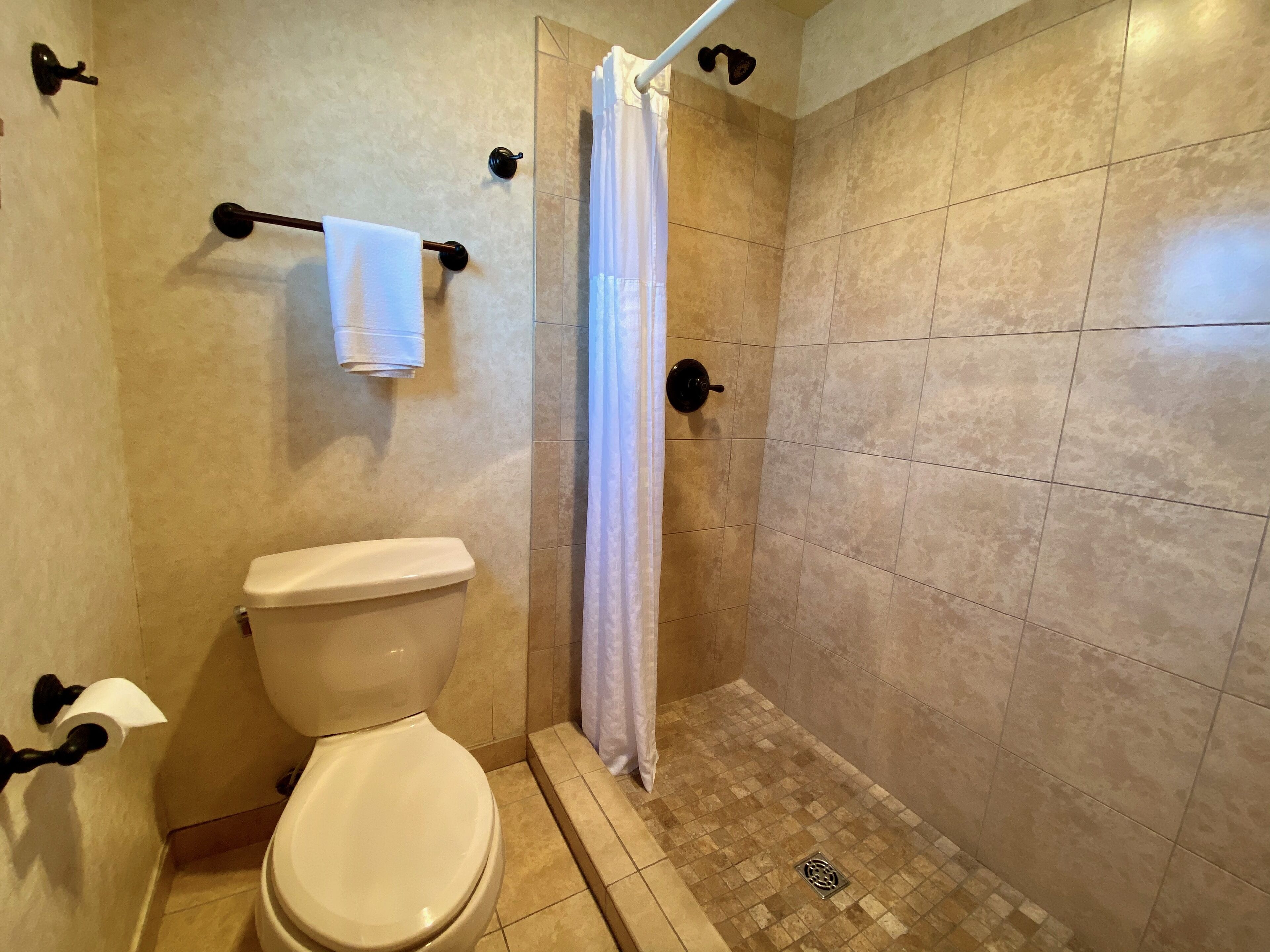 A bathroom with a toilet, a shower with a curtain, and a towel rack.