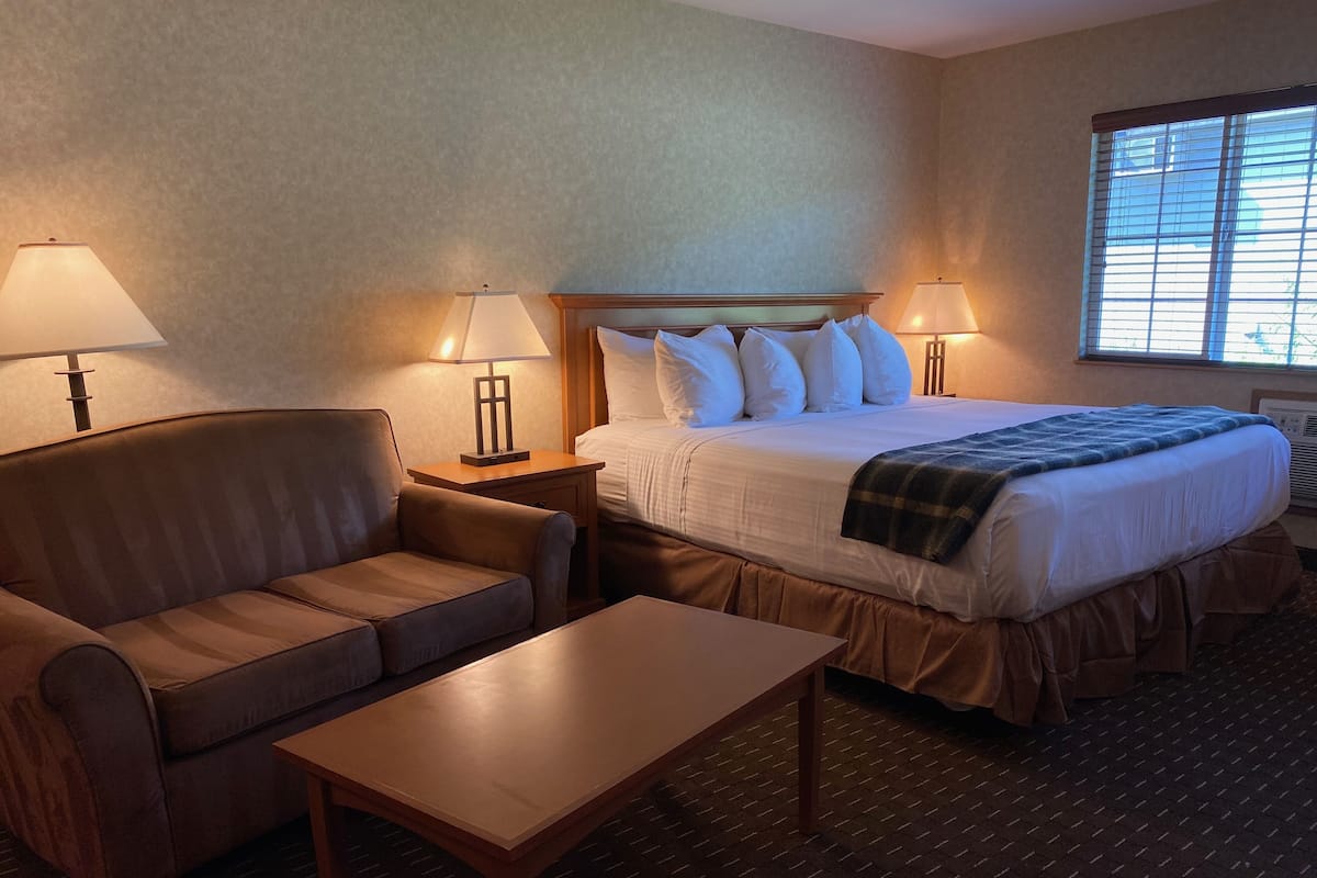 Una camera d'albergo con un letto, un divano, un tavolo e due lampade ai comodini.