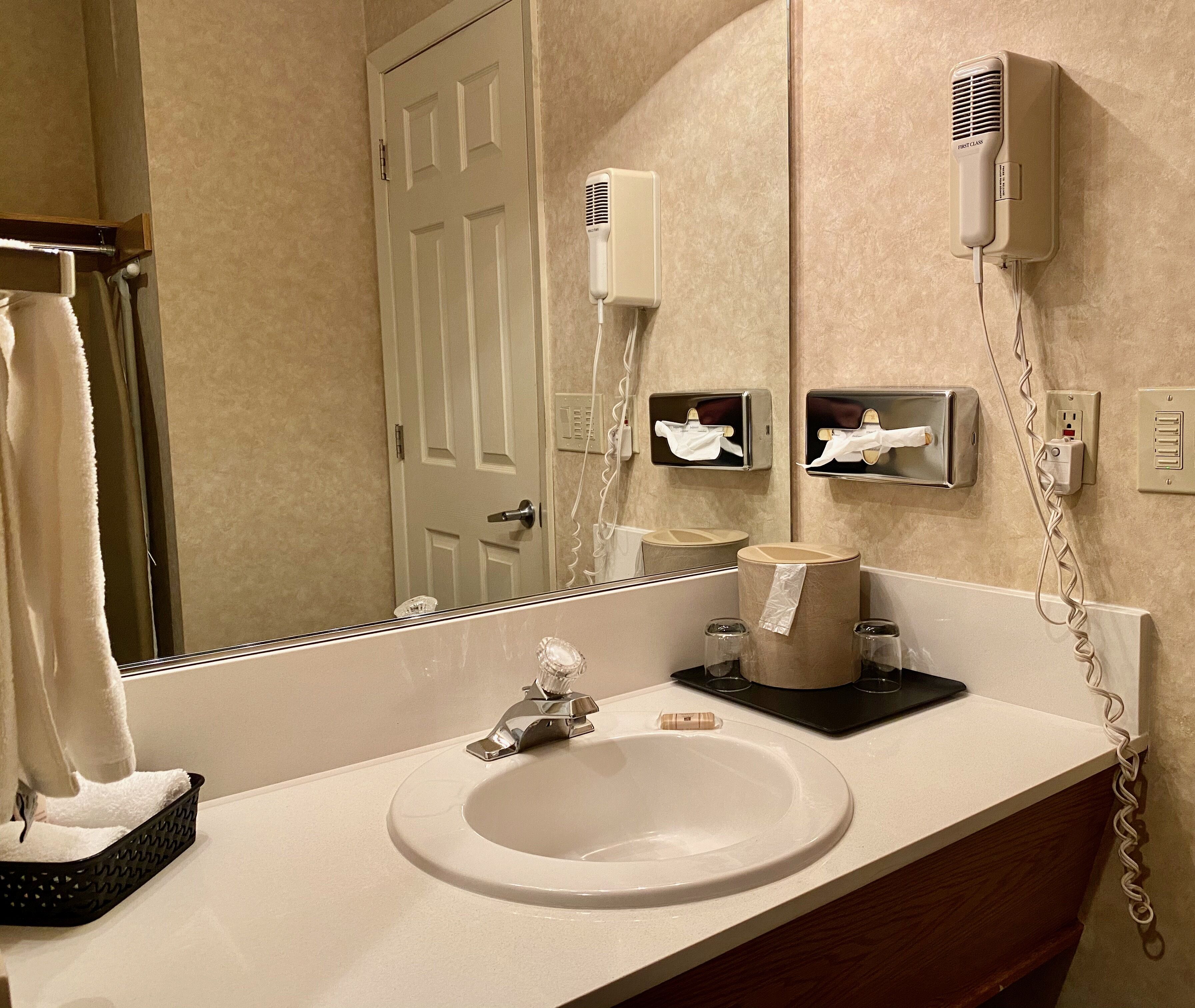 A bathroom with a sink, mirror, towel dispenser, and hair dryer.