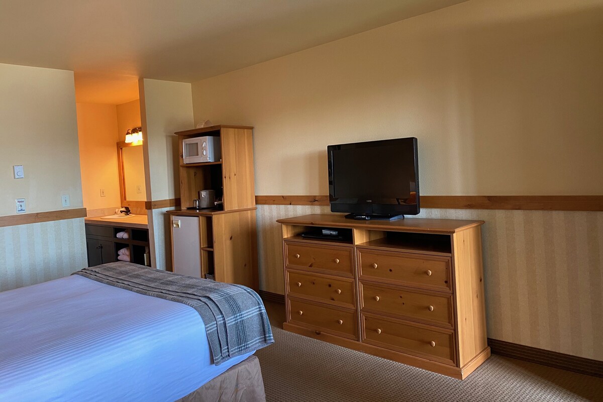 A hotel room with a bed, wooden dresser, television, microwave, and a small kitchenette.