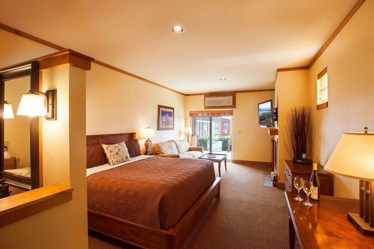 A hotel room with a large bed, a desk, a chair, a TV, and a window.