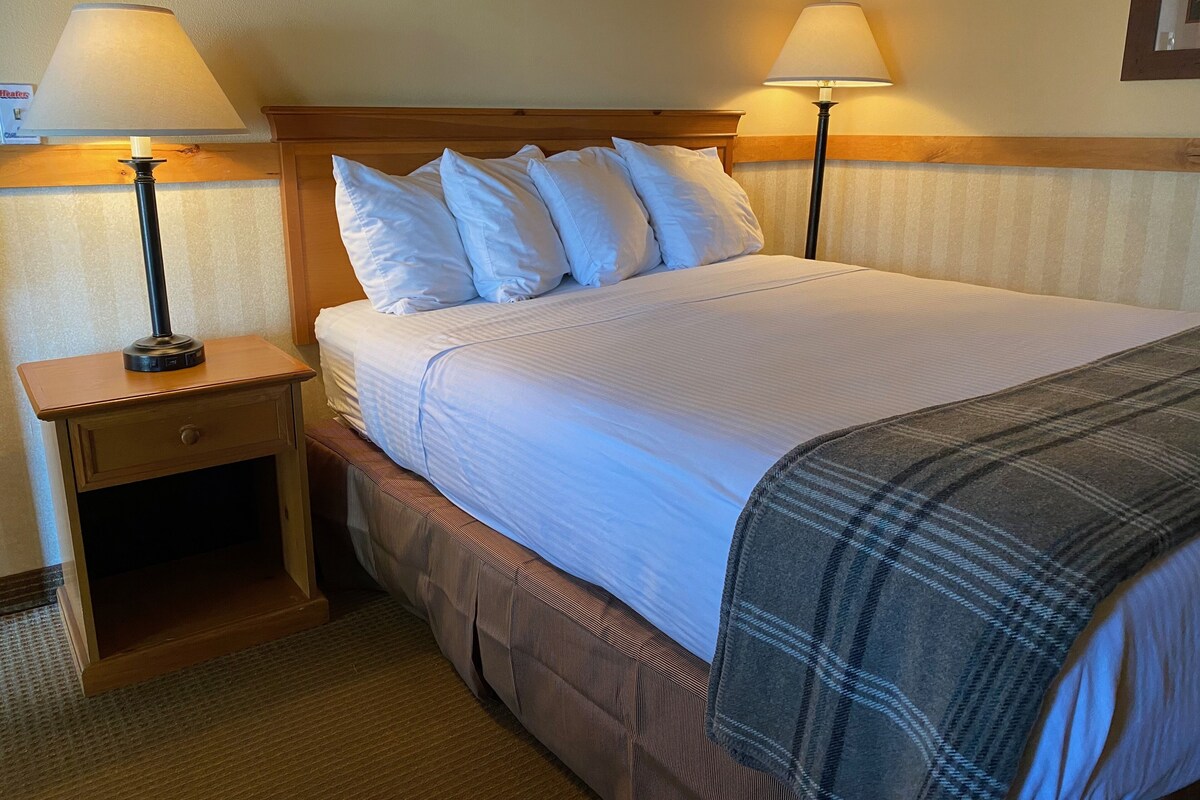 A neatly made bed with white linens, a wooden headboard, and two bedside lamps.