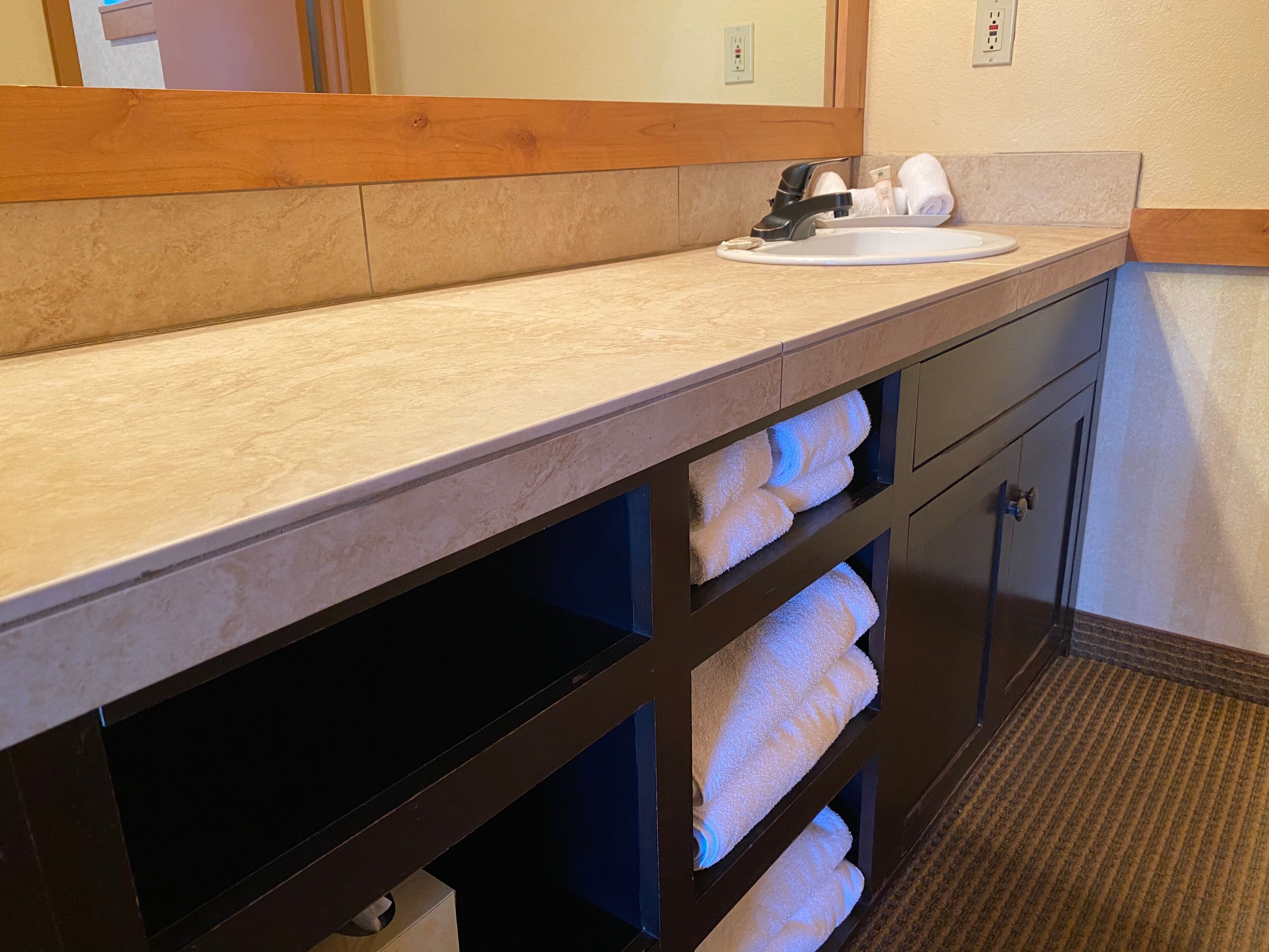 Une salle de bain avec un comptoir beige, un lavabo, un miroir et un porte-serviettes avec des serviettes.