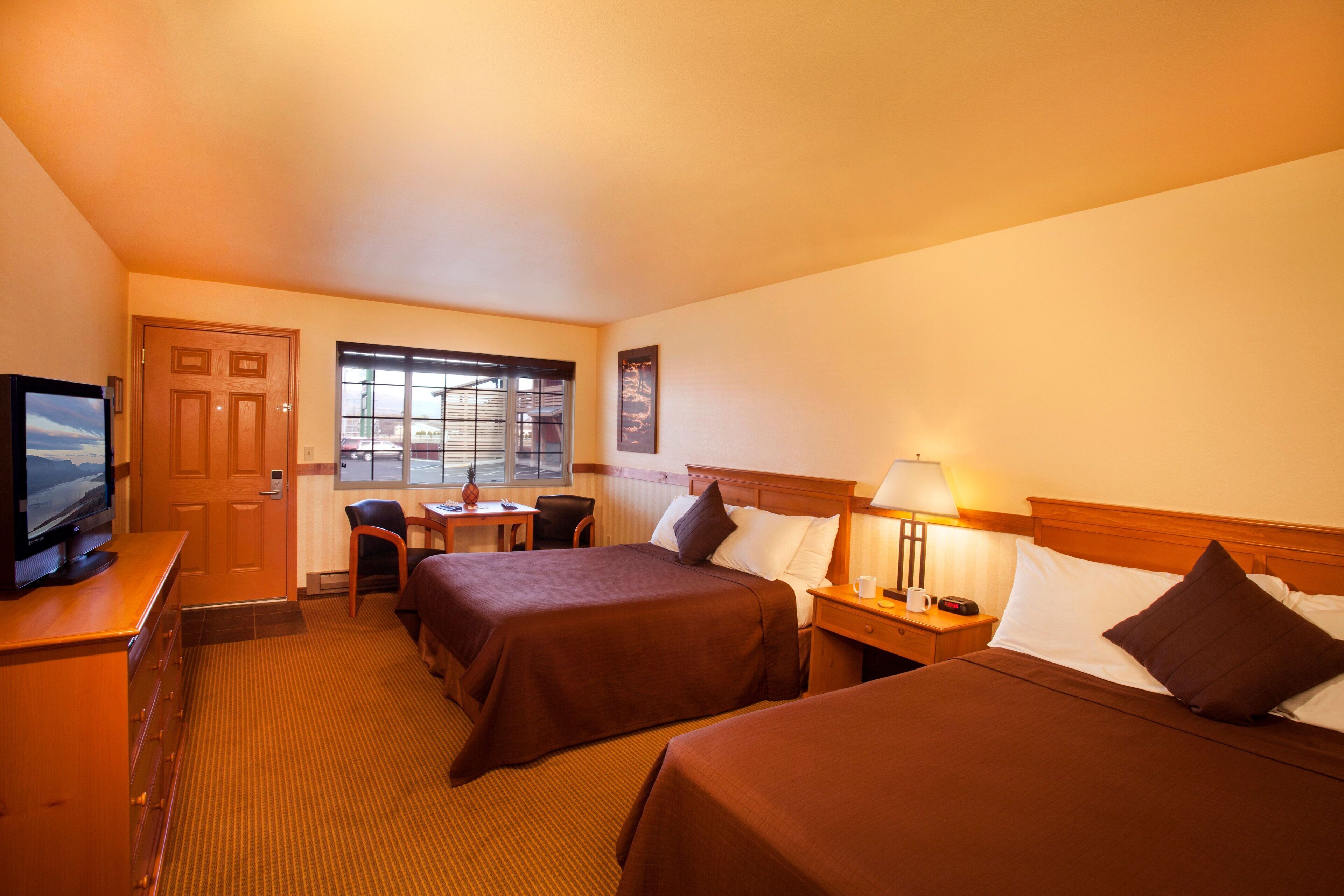 A hotel room with two beds, a desk, a chair, a television, and a window with blinds.
