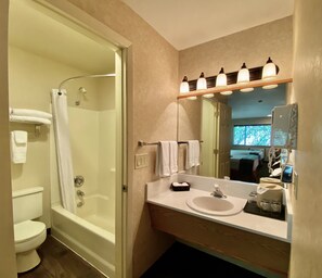 A bathroom with a shower, toilet, sink, and mirror.