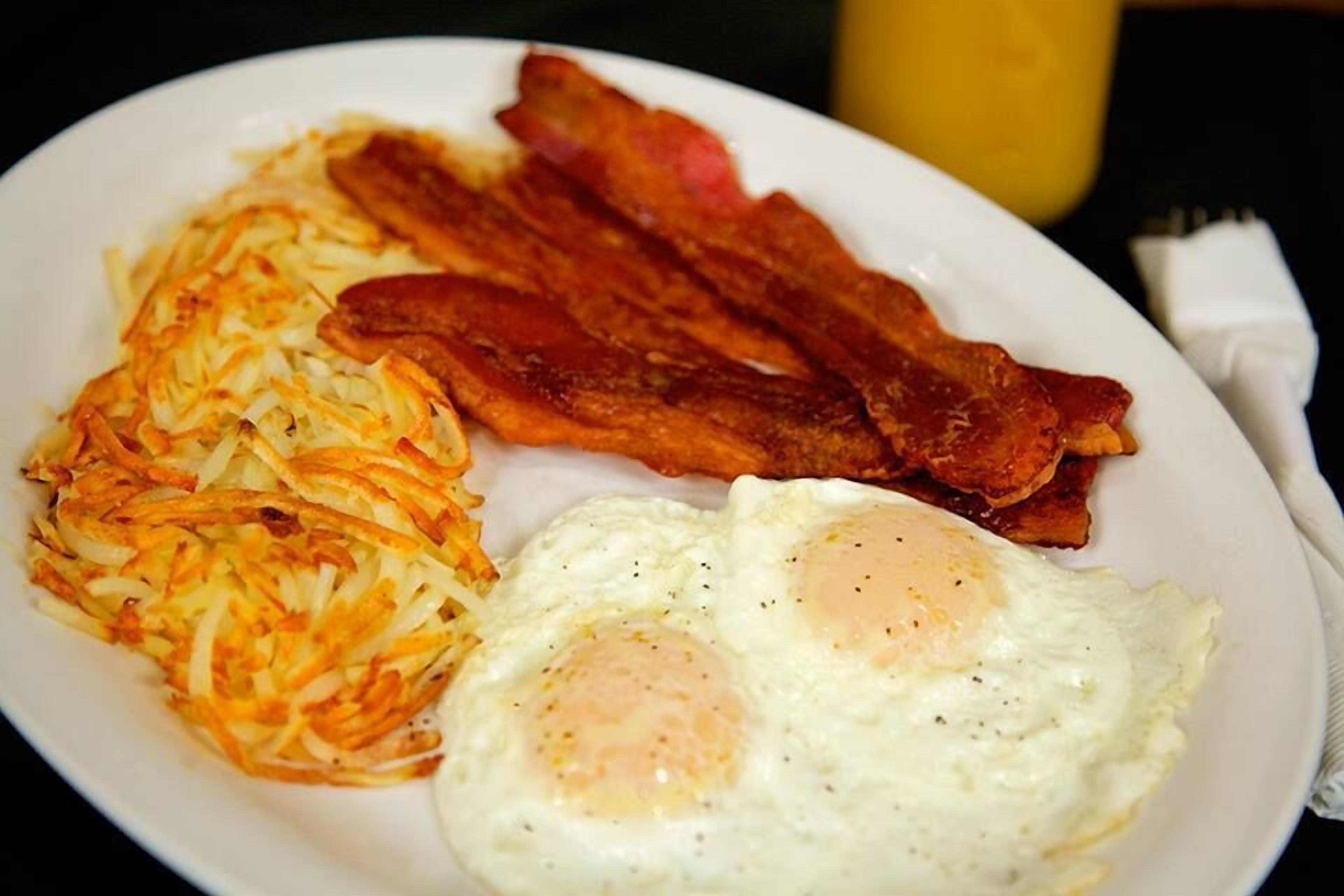 A plate with hash browns, bacon, and fried eggs.