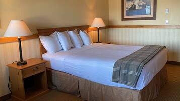 A hotel room with a large bed, two bedside lamps, a nightstand, a wooden headboard, a framed picture on the wall, and a carpeted floor.