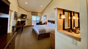 A spacious bedroom with a large bed, a desk, a television, and a bathroom with a mirror and lights. - Cousins Country Inn (The Dalles)