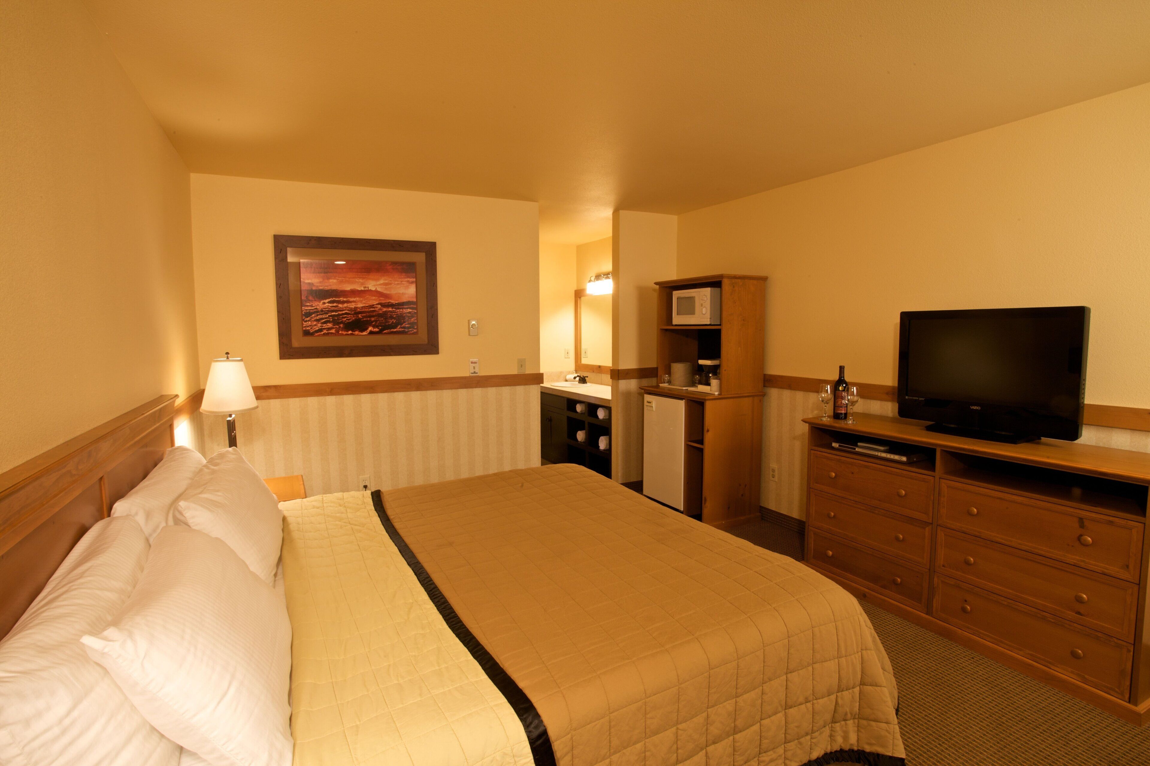 Habitación de hotel con una cama grande, televisión, microondas y una kitchenette pequeña.