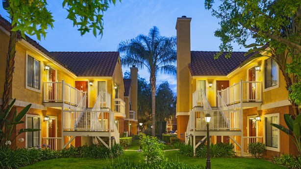 A courtyard with two-story buildings, a central palm tree, and a well-maintained lawn. - Clementine Hotel & Suites Anaheim (Anaheim)