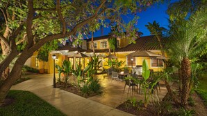 A well-lit patio area with outdoor seating and a dining table, surrounded by lush greenery and a large tree. - Clementine Hotel & Suites Anaheim (Anaheim)