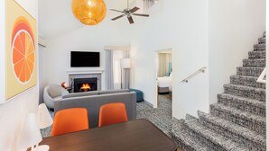A modern hotel room with a fireplace, a sofa, a dining table, and a staircase with patterned carpet. - Clementine Hotel & Suites Anaheim (Anaheim)
