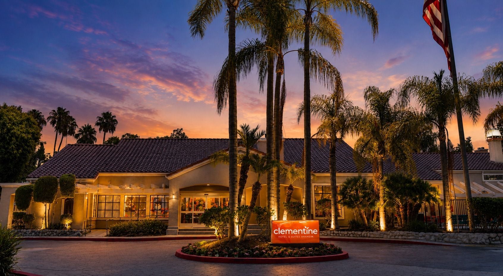 A hotel with a tiled roof, palm trees, and a sign reading 'Clementine Hotel & Suites Anheim.'
