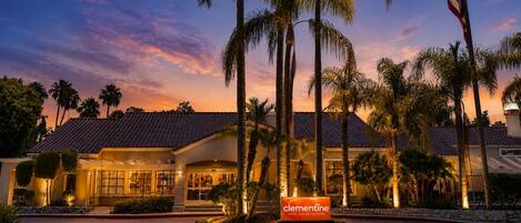 A hotel with a tiled roof, palm trees, and a sign reading 'Clementine Hotel & Suites Anheim.'