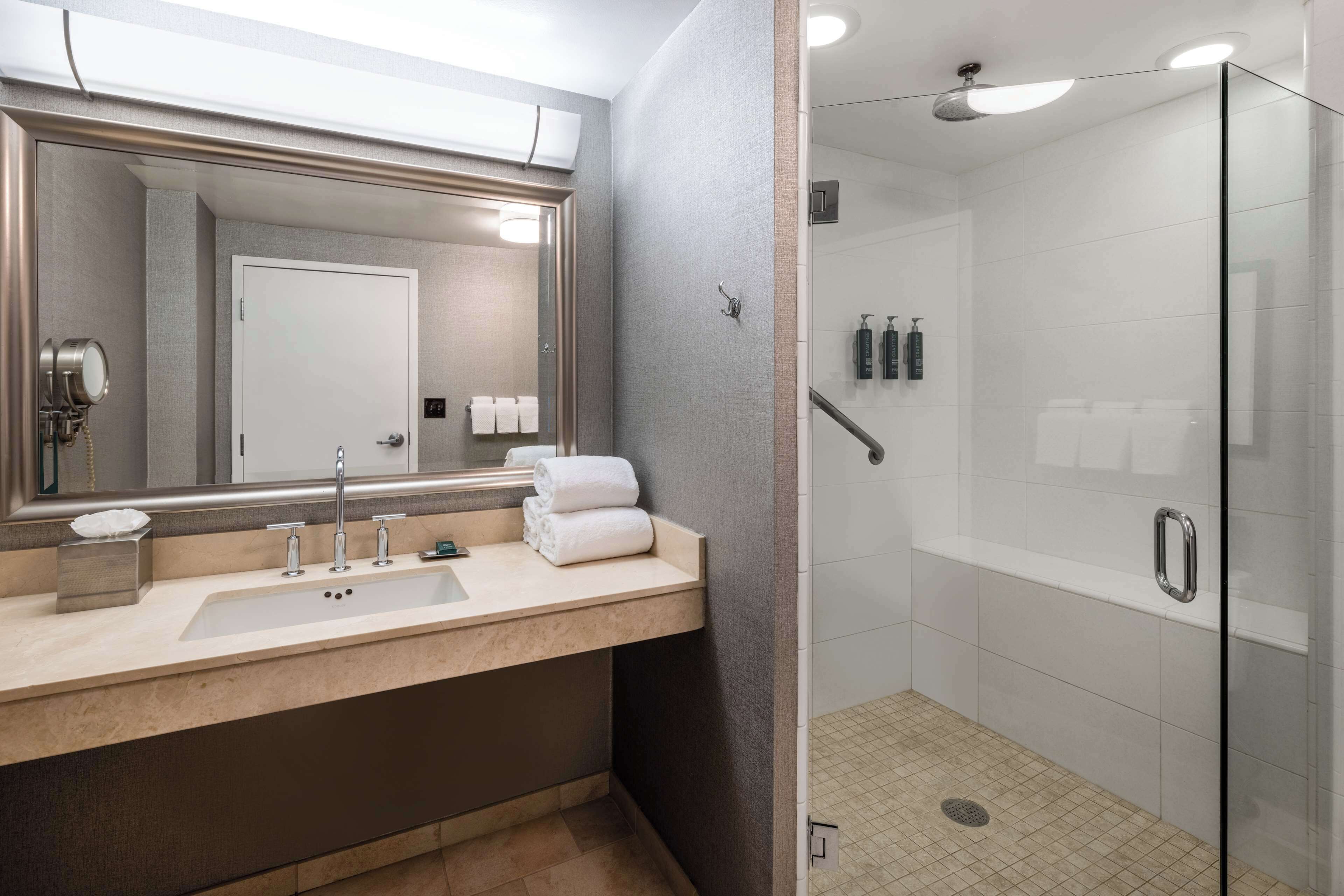 Un baño moderno con un espejo grande, un lavamanos y cabina de ducha con mampara de vidrio.