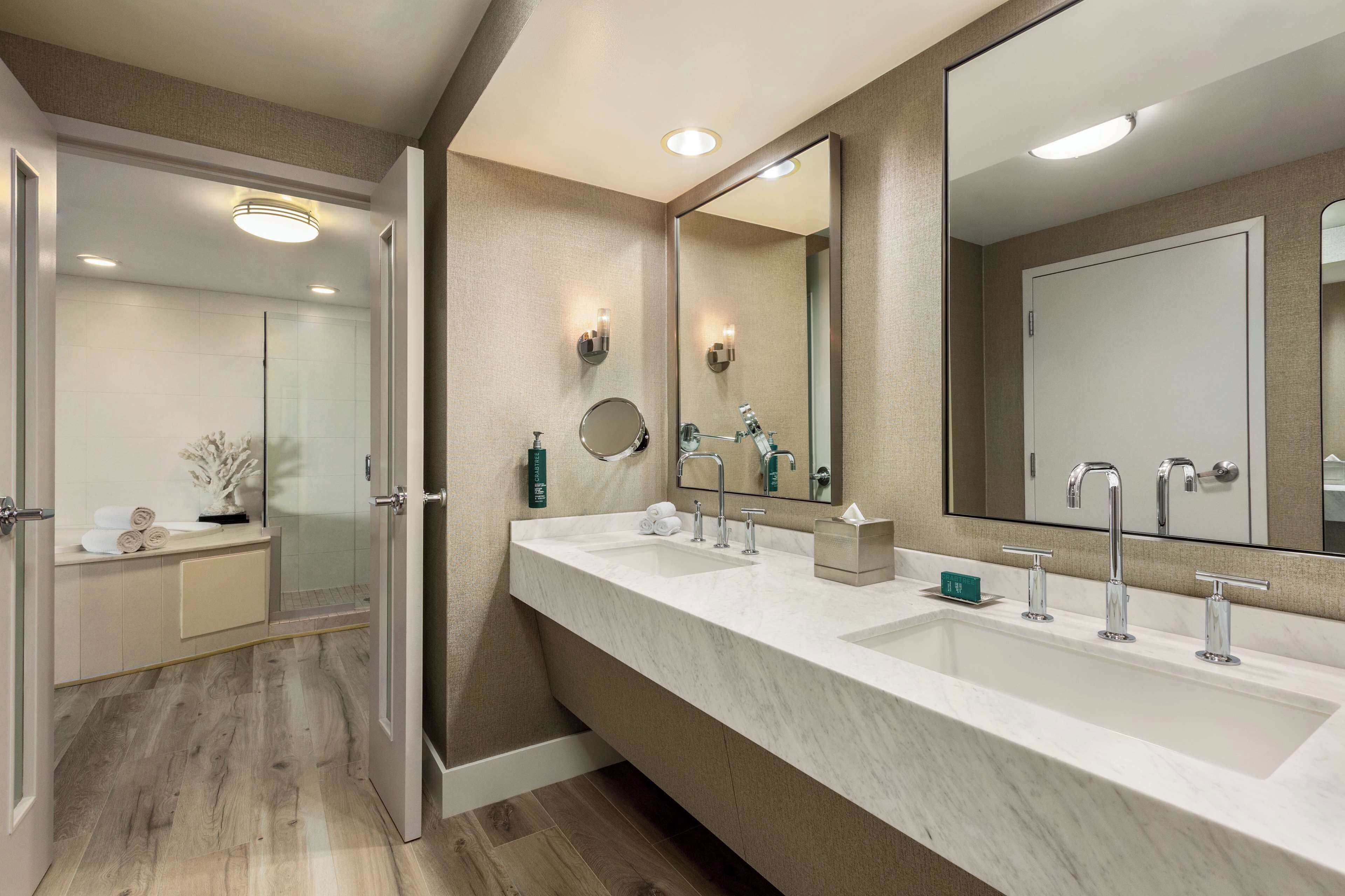 A modern bathroom with two sinks, a large mirror, and a glass shower enclosure.
