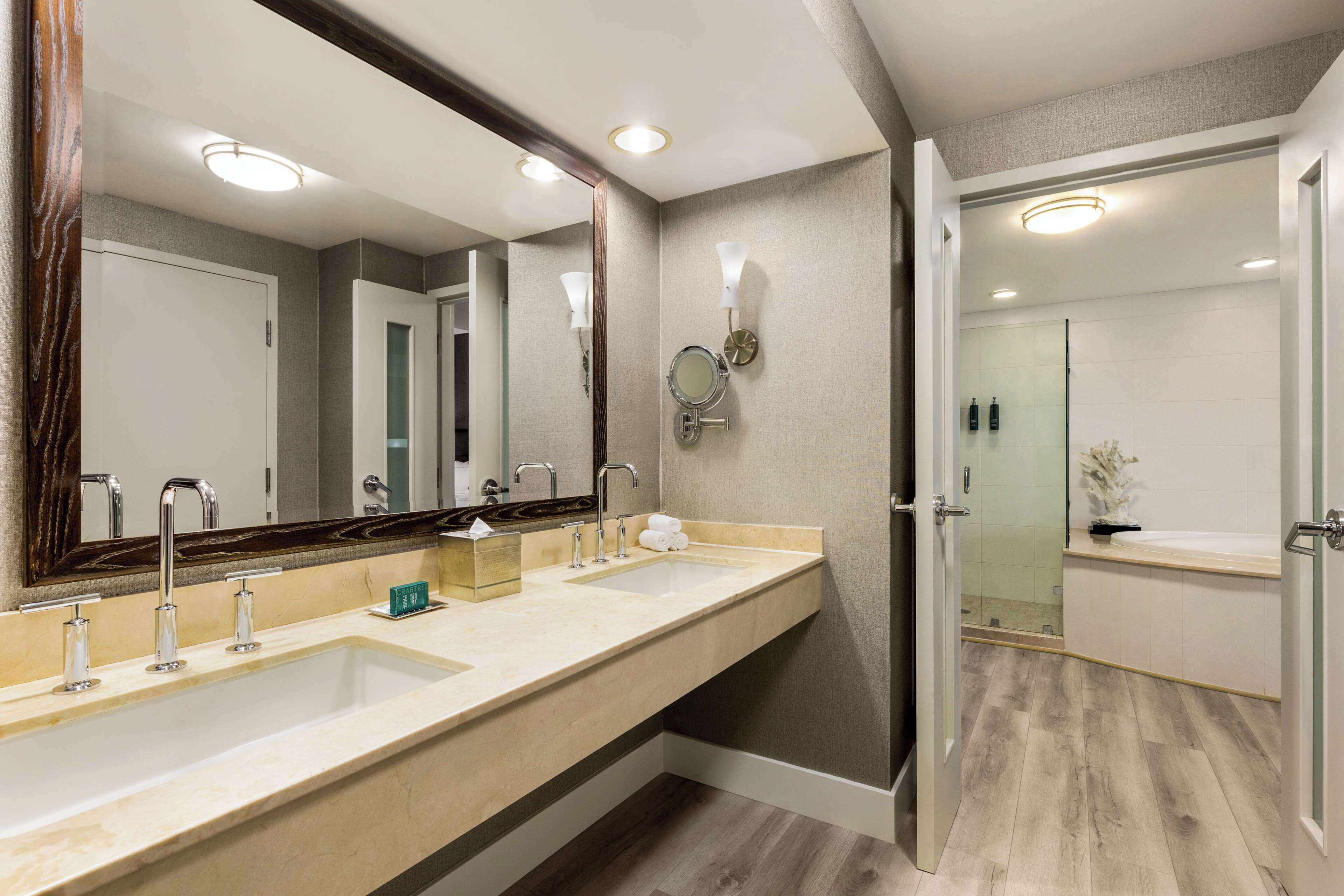 A modern bathroom with a large mirror, two sinks, and a shower area.