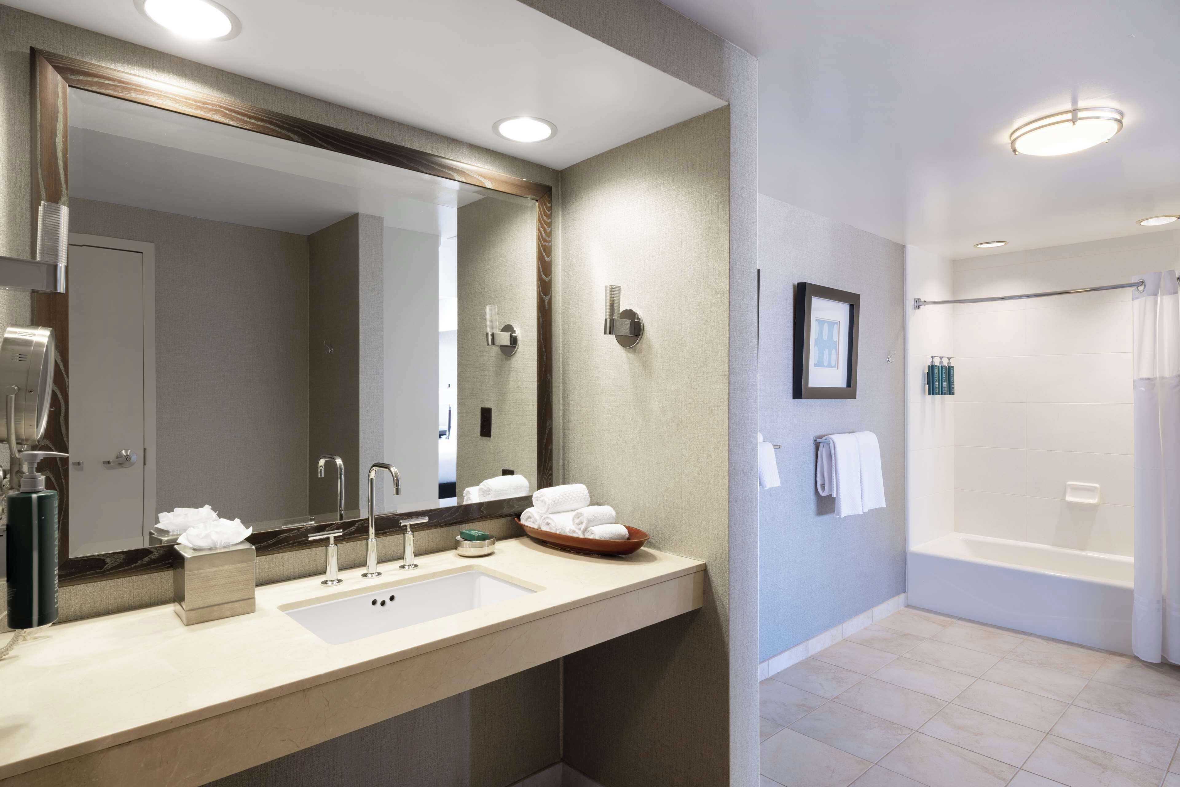 A modern bathroom with a large mirror, dual sinks, a bathtub, and a shower area.