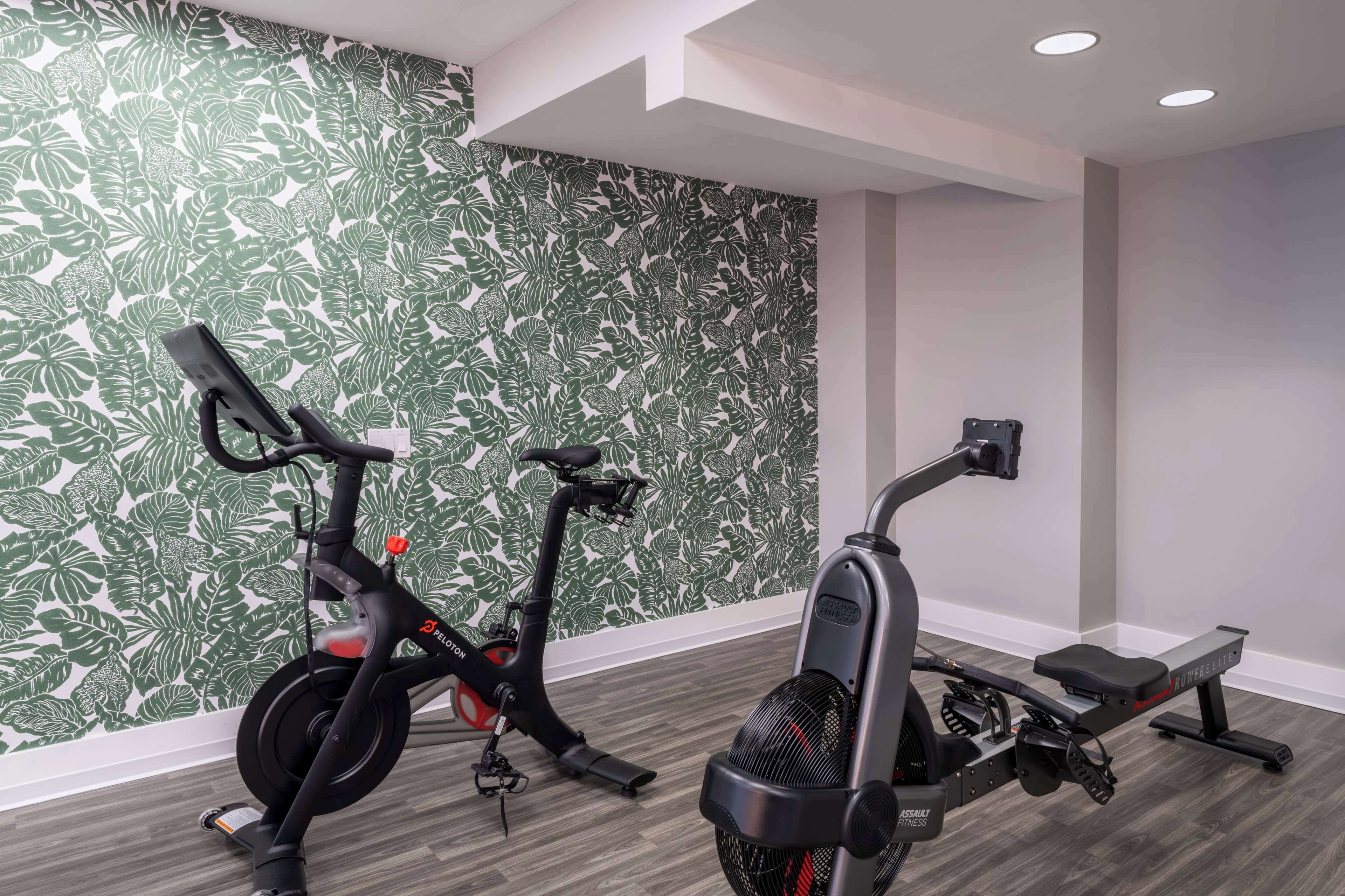 A room with a stationary bike and an elliptical machine, a patterned wall, and a wooden floor.