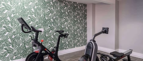 A room with a stationary bike and an elliptical machine, a patterned wall, and a wooden floor.