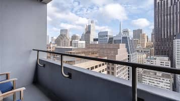 Varanda com grade de metal, vista para um horizonte urbano com diversos edifícios e duas cadeiras azuis com almofadas.
