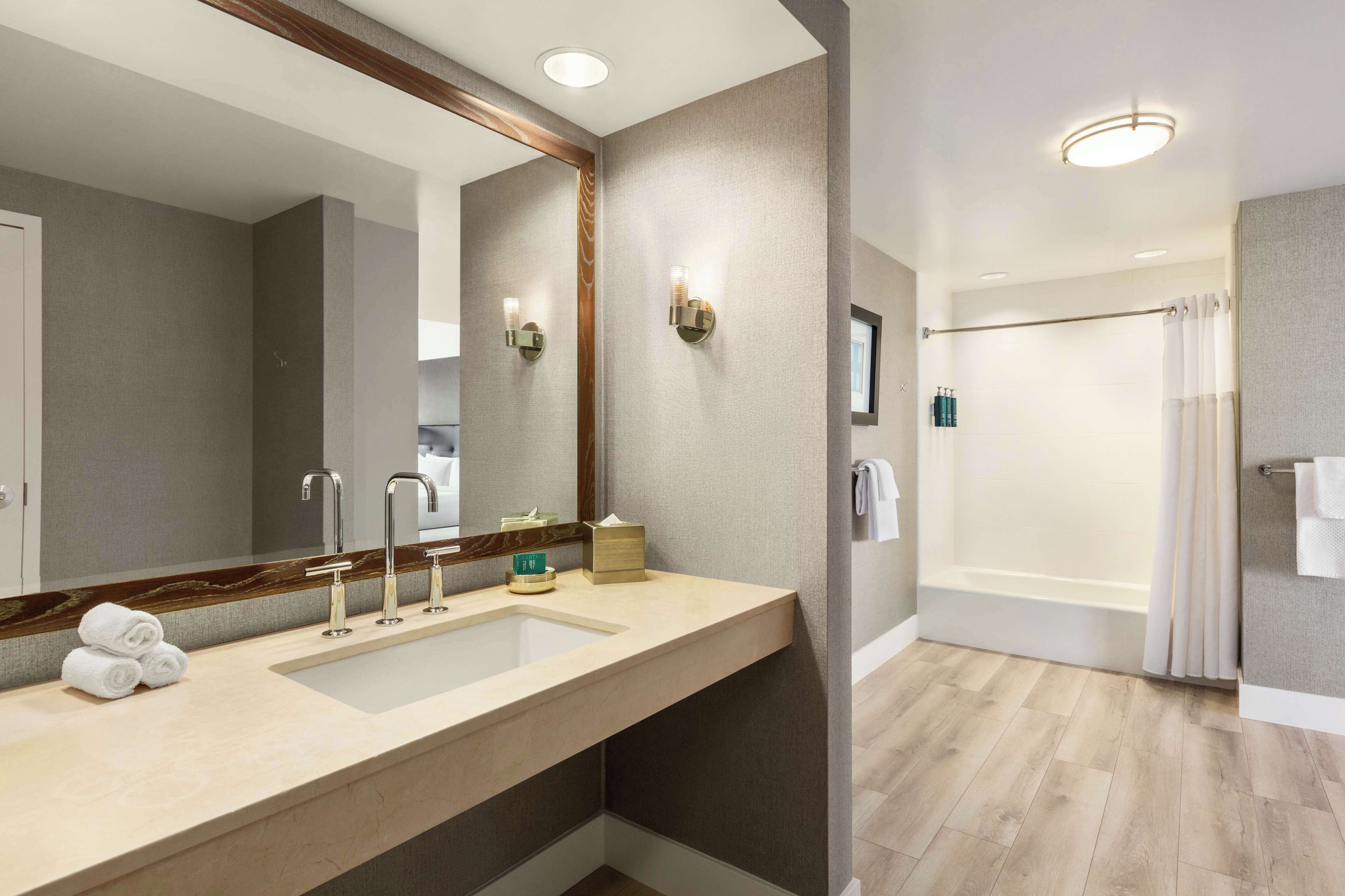 A modern bathroom with a large mirror, a sink with two faucets, and a shower area.