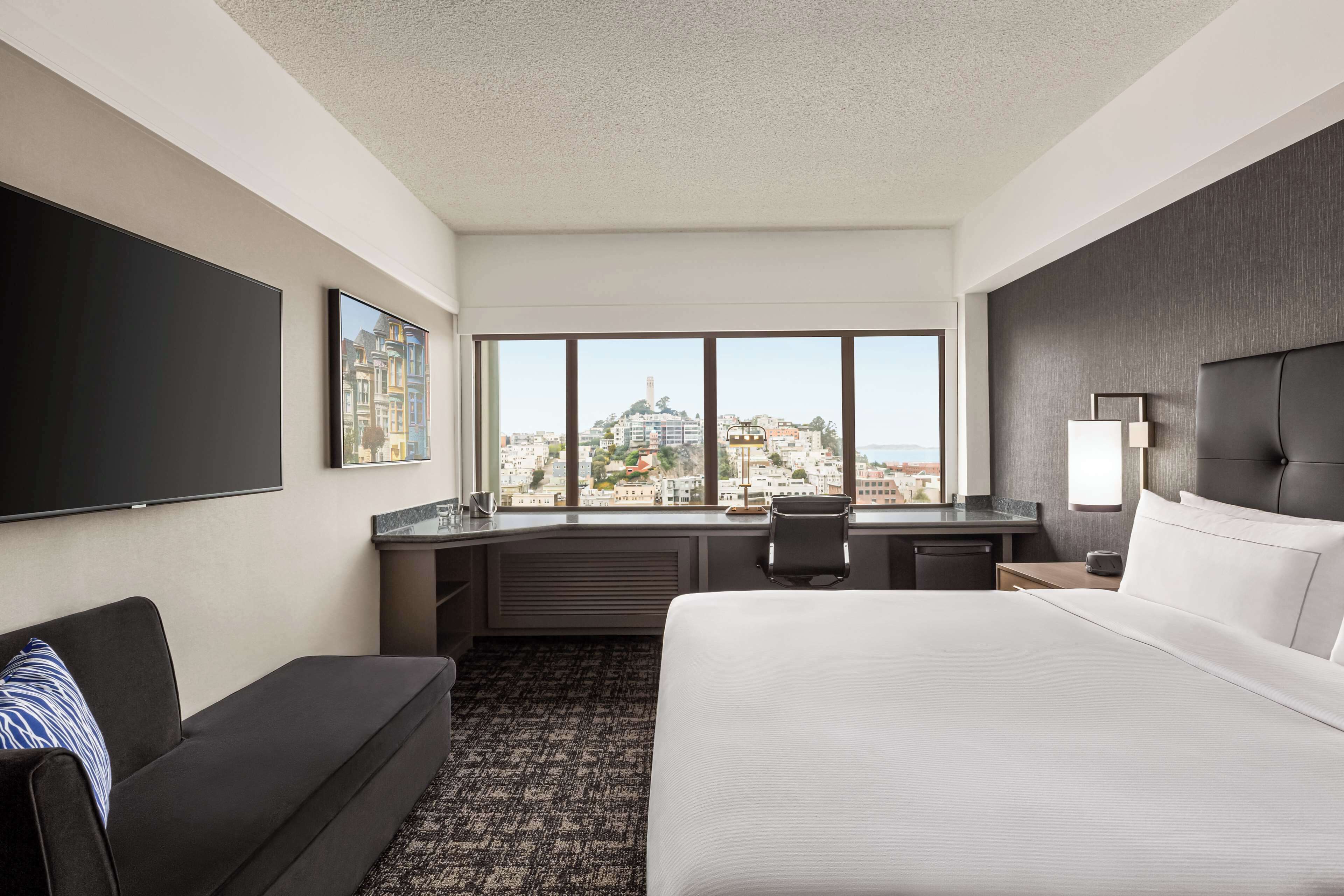 Una habitación de hotel con una cama grande, un escritorio, una silla, un televisor y una ventana con vistas a la ciudad.