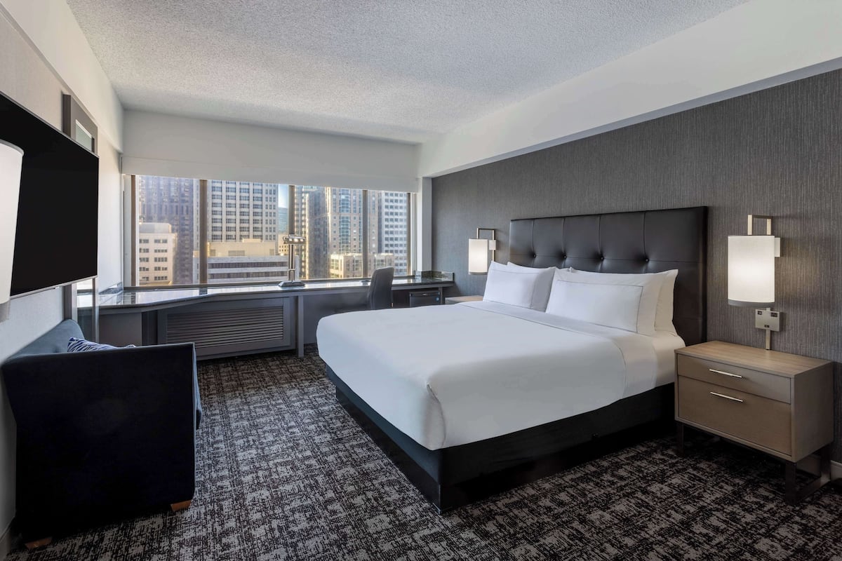 A hotel room with a large bed, a desk, a chair, and a TV.