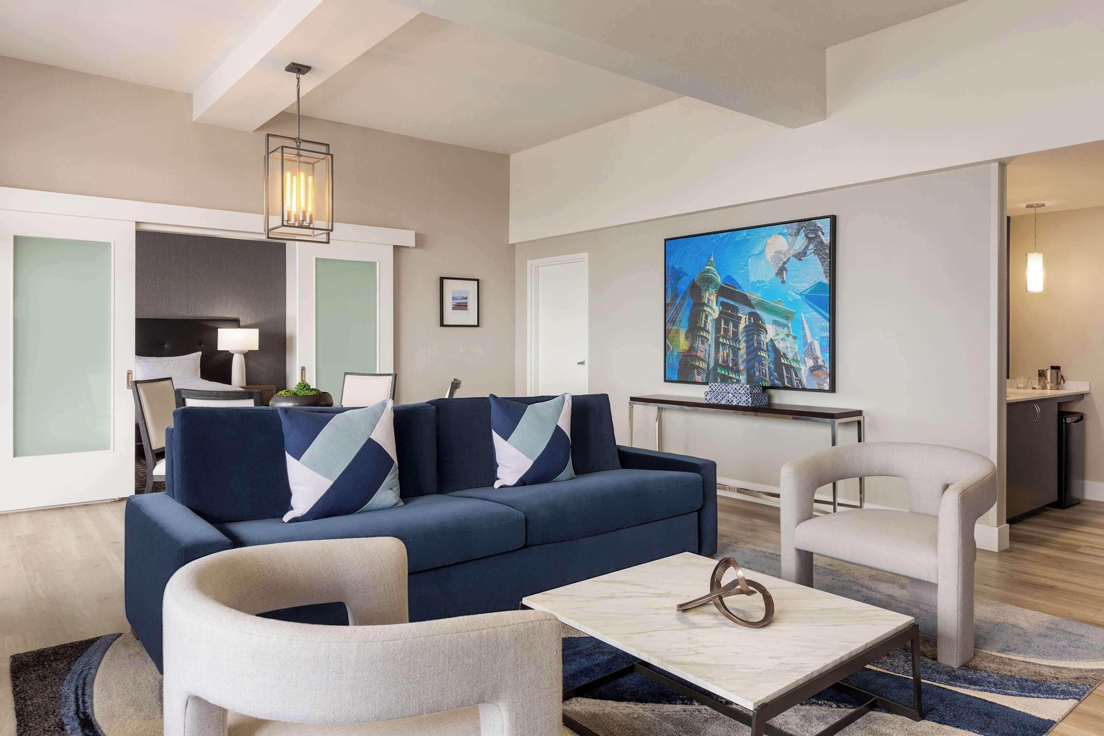 A modern living room with a sofa, armchairs, a coffee table, and a painting on the wall.