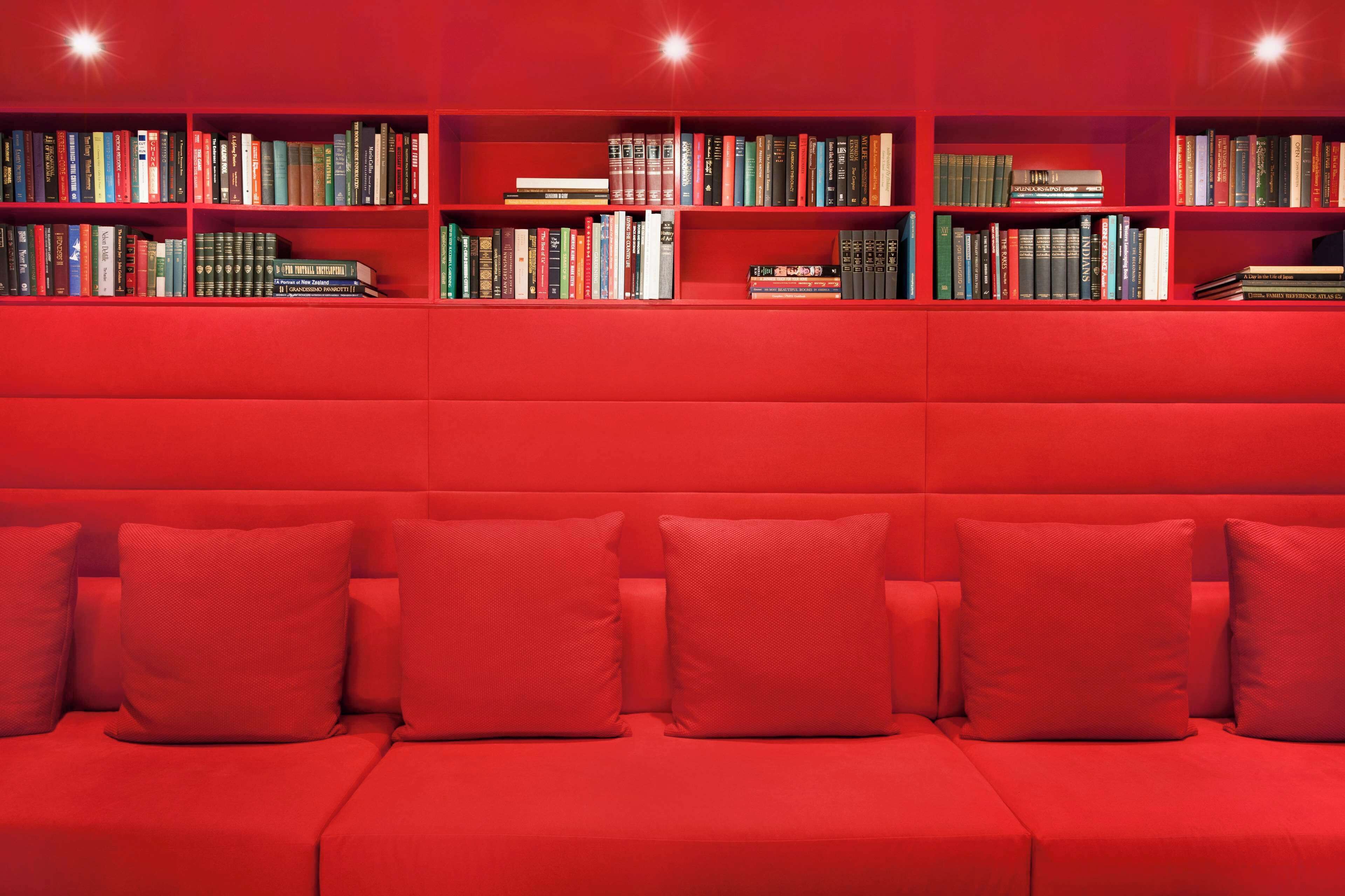 A red sofa with matching cushions and a bookshelf filled with books.