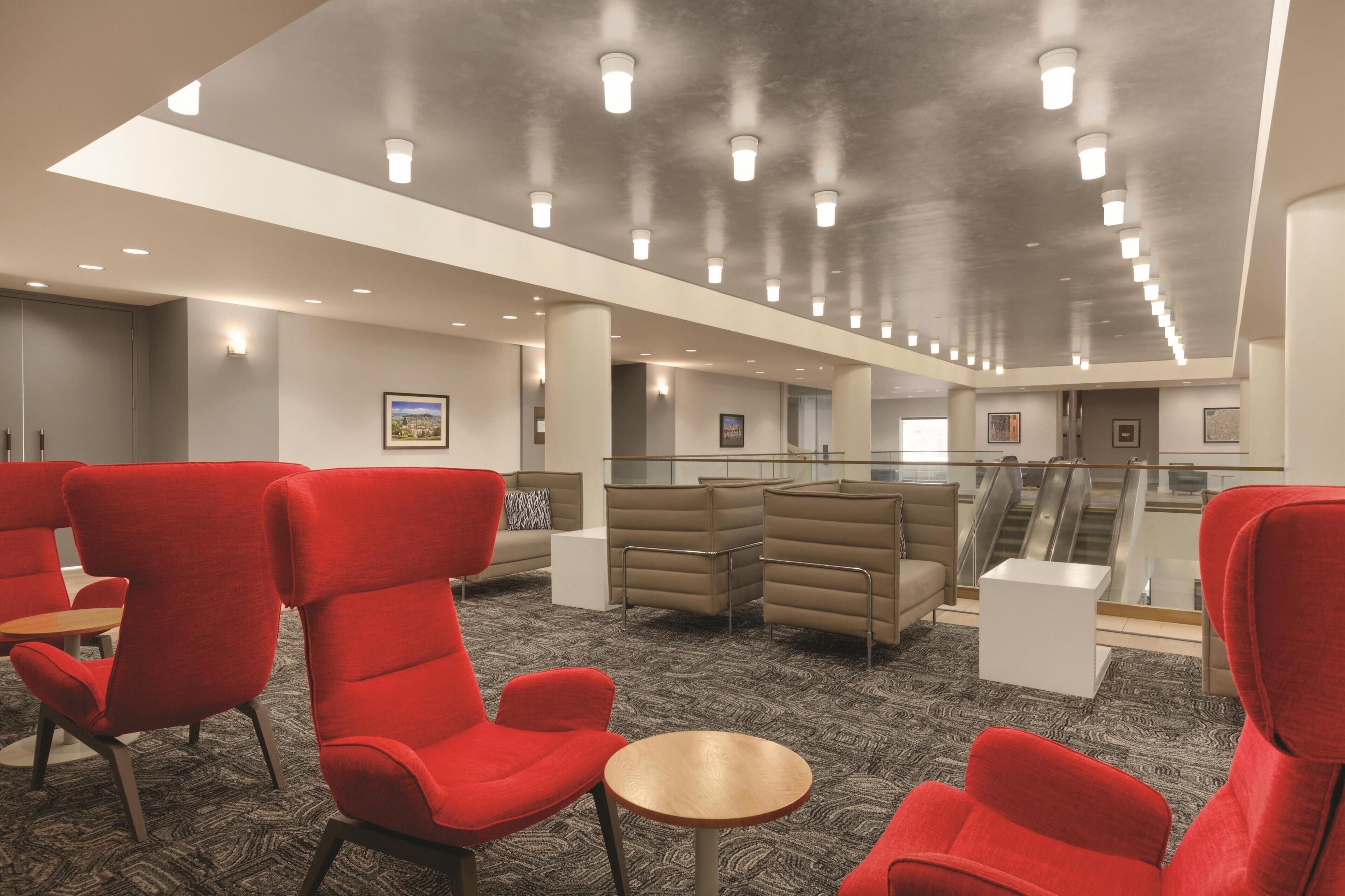 A spacious lobby with red and beige seating, a glass railing, and a staircase.