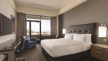 A hotel room with a large bed, a desk, a chair, a TV, and a window with curtains.