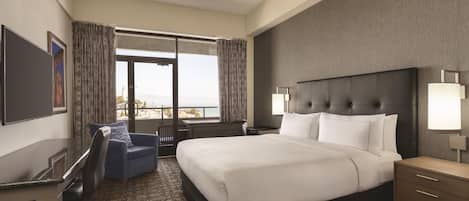A hotel room with a large bed, a desk, a chair, a TV, and a window with curtains.
