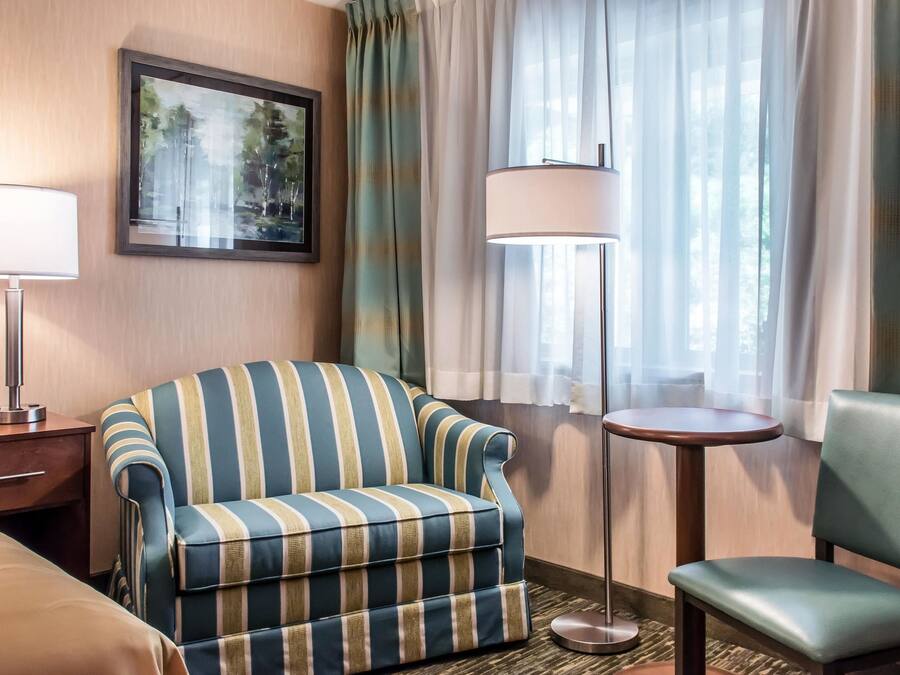 A hotel room with a striped armchair, a small round table, a lamp, and a bed.