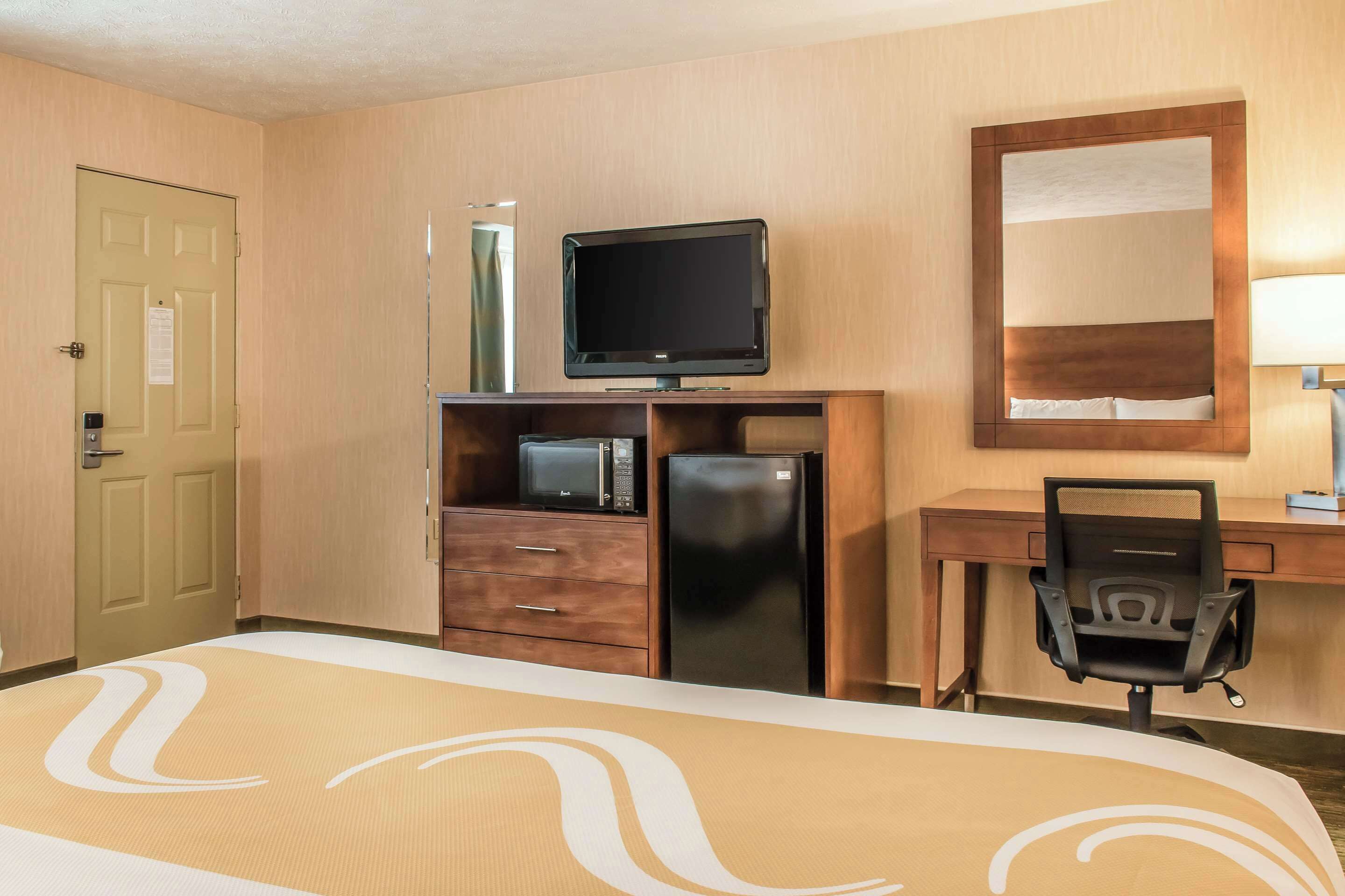 A hotel room with a bed, a desk with a chair, a television, a refrigerator, and a microwave.