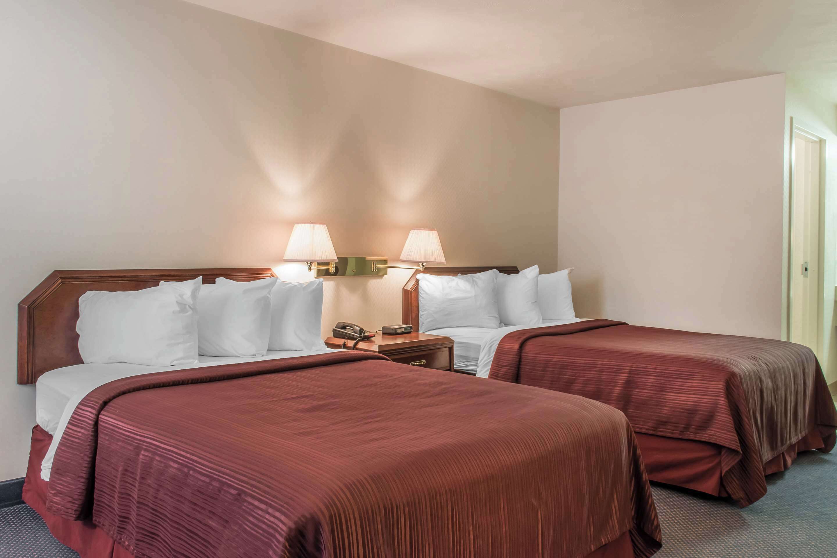 Habitación de hotel con dos camas, cabecero de madera, mesita de noche con lámpara y teléfono.