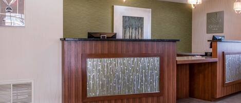 A reception desk with a wooden finish and a glass panel, a framed artwork above it, and a sign for 'Choice Hotels International'.