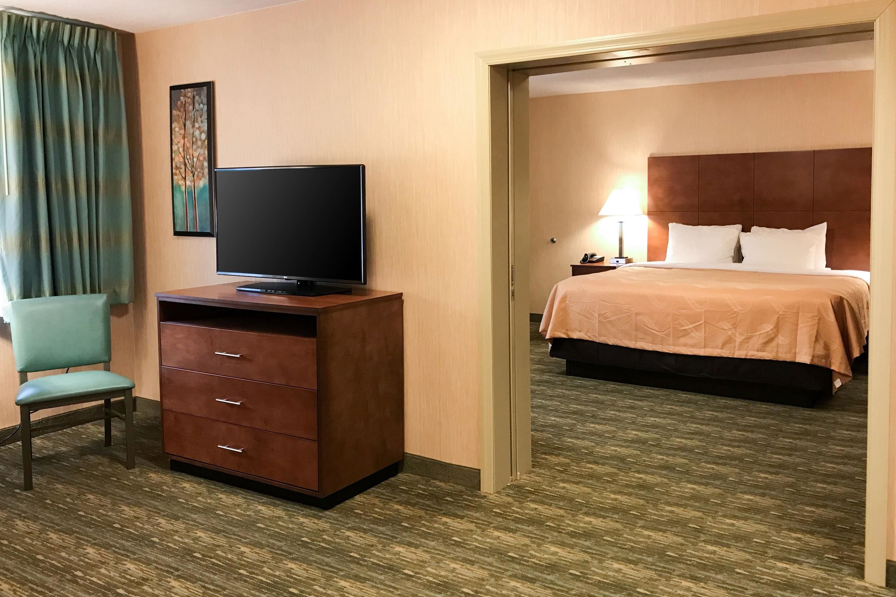 Una habitación de hotel con una televisión sobre un aparador de madera, una cama con cabecero y una silla.