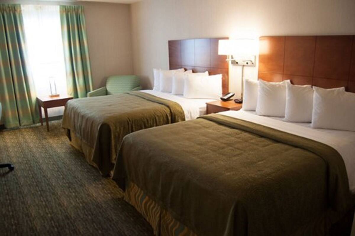 A hotel room with two beds, a desk, a chair, a lamp, and a nightstand.