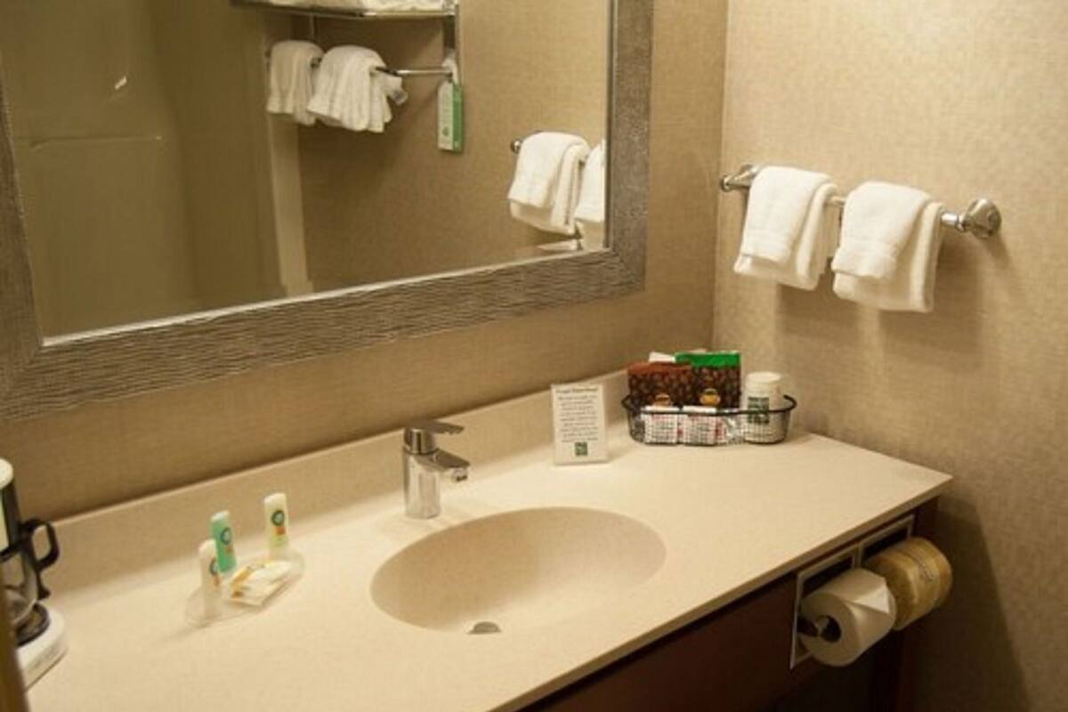 A bathroom with a sink, mirror, towel rack, and toiletries.