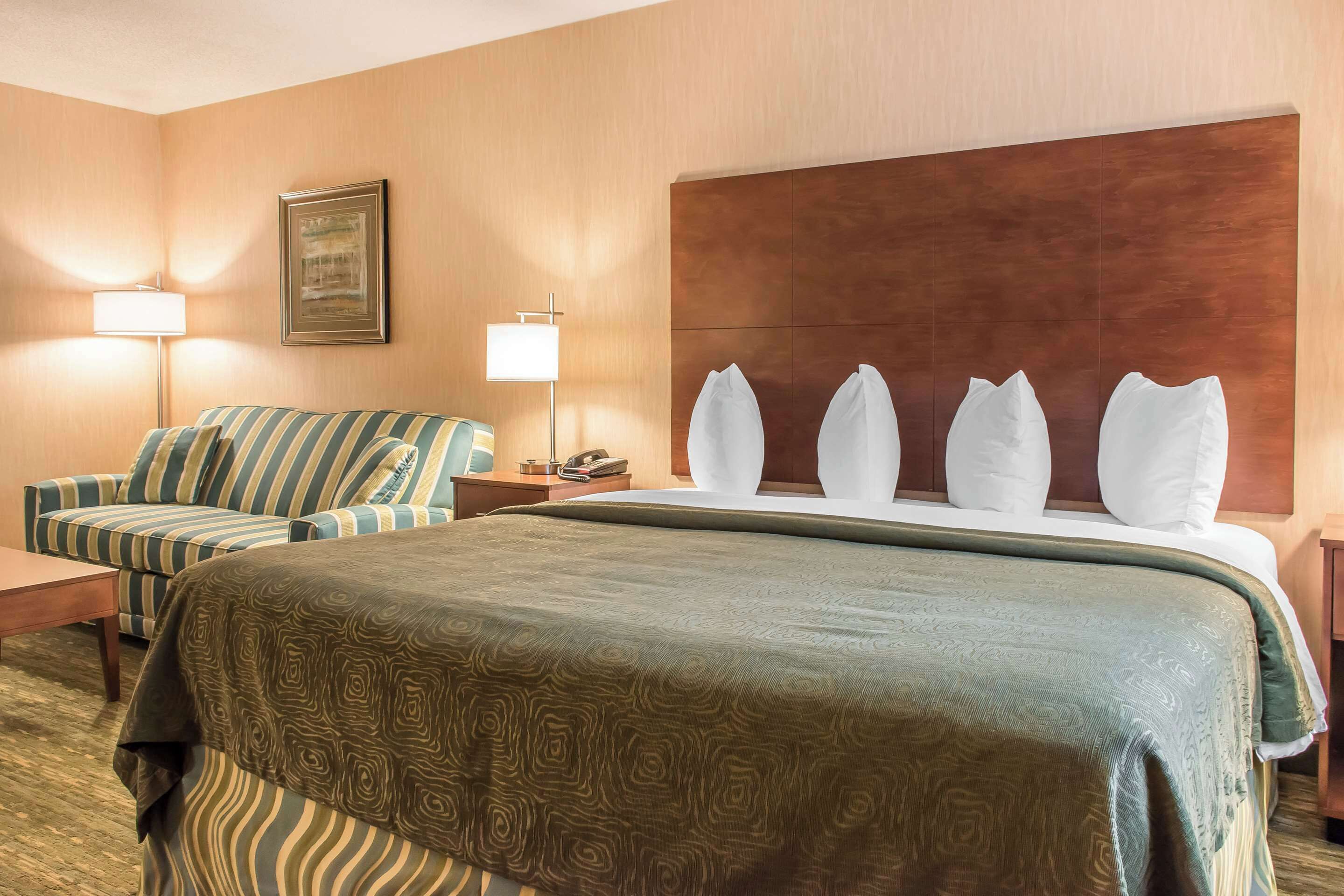 A hotel room with a large bed, a striped sofa, a desk, and a lamp.