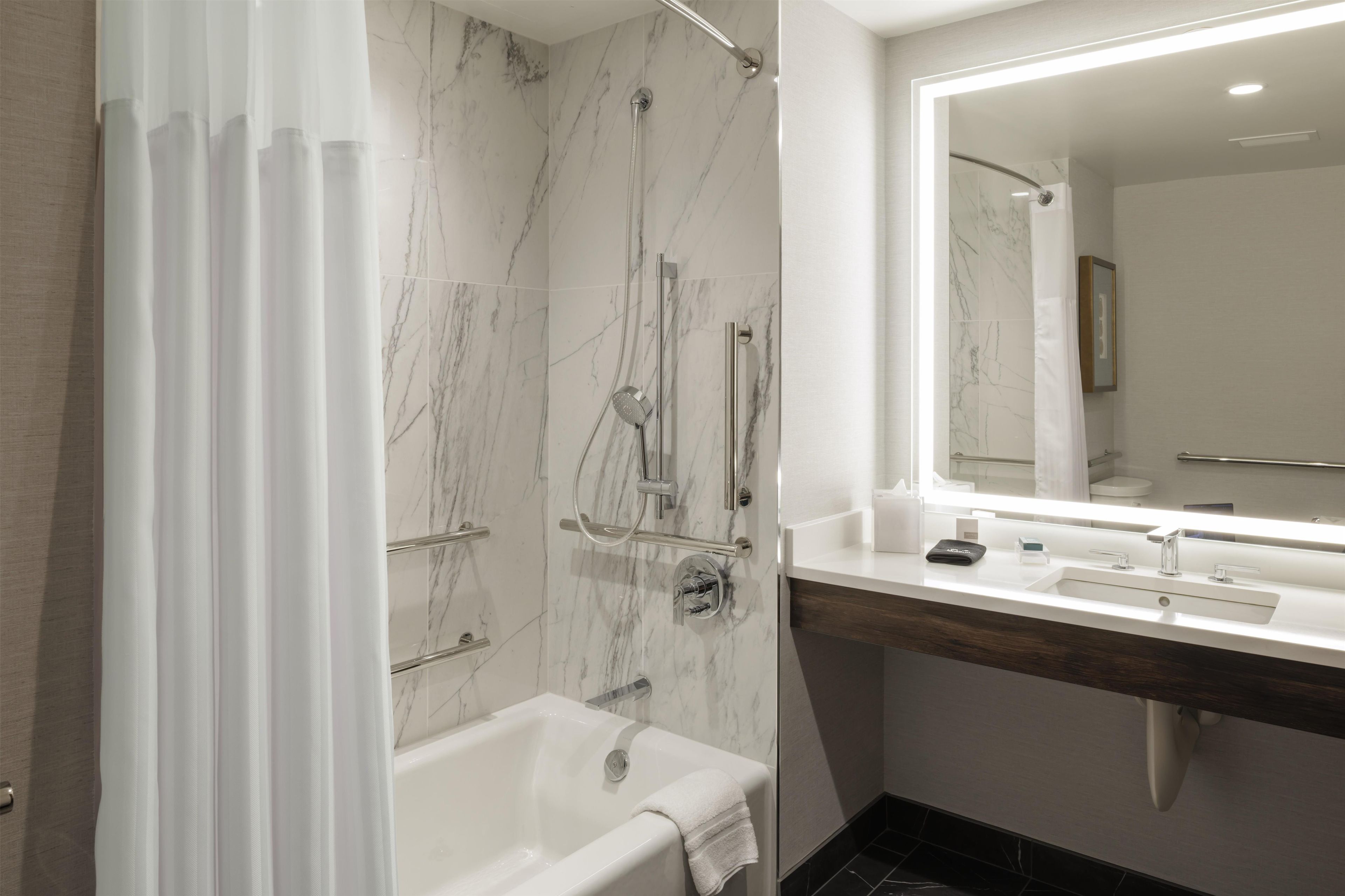 A modern bathroom with a marble shower, a bathtub, and a vanity with a mirror.