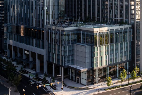A modern building with a glass facade, a visible entrance, and a street view with traffic lights. - Hilton Arlington Rosslyn The Key (Arlington)