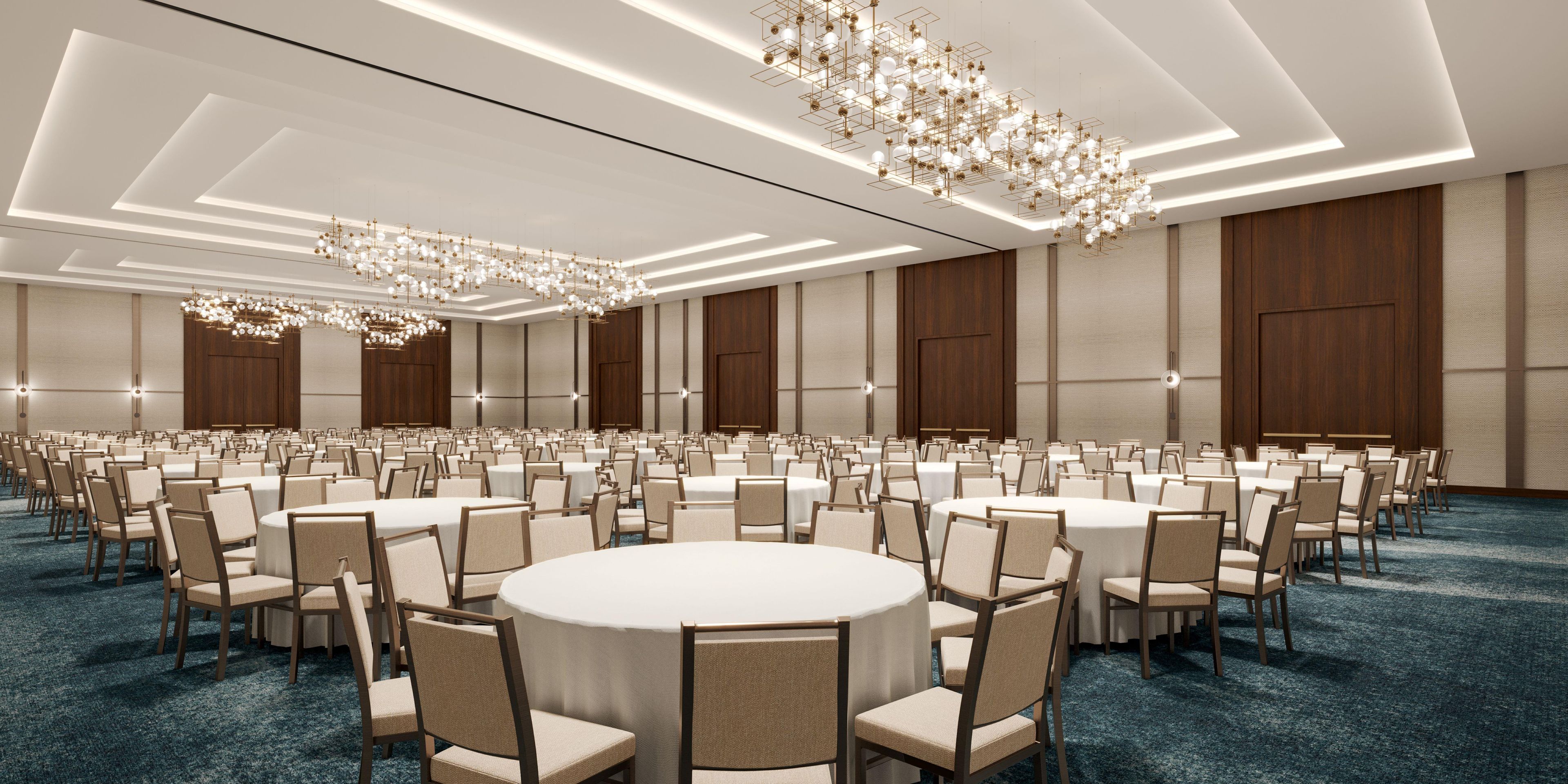 A large conference room with round tables and chairs, modern chandeliers, and wooden paneling.